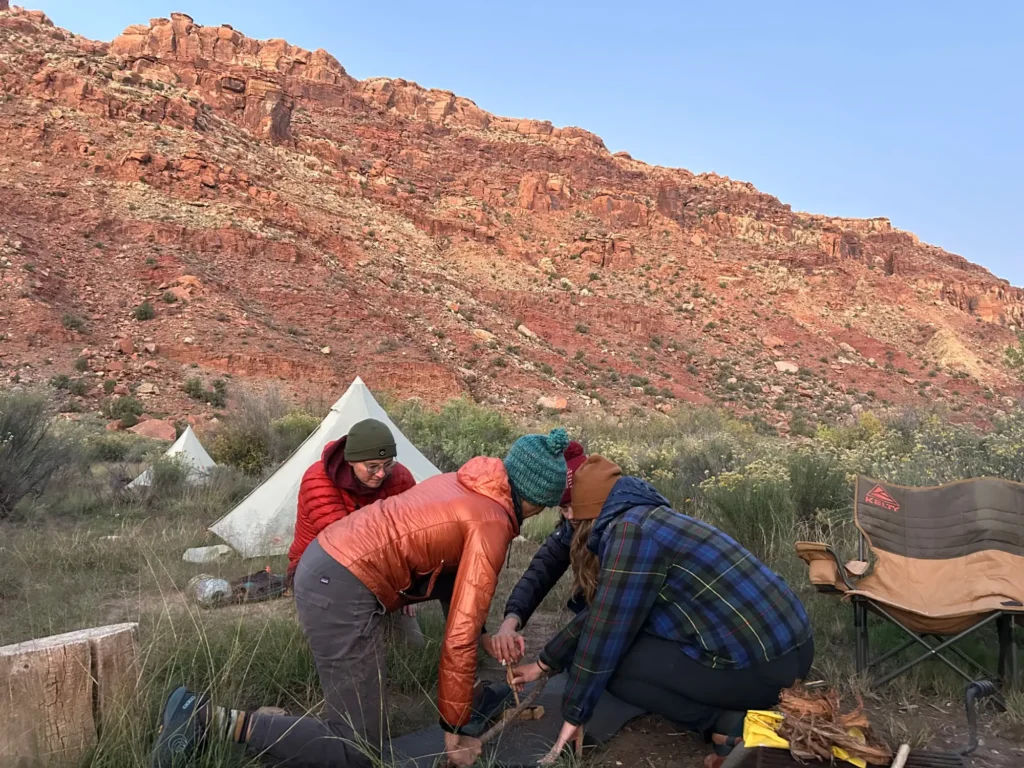 Participants working together on a bow-drill fire beneath red canyon walls at a LifeWays camp