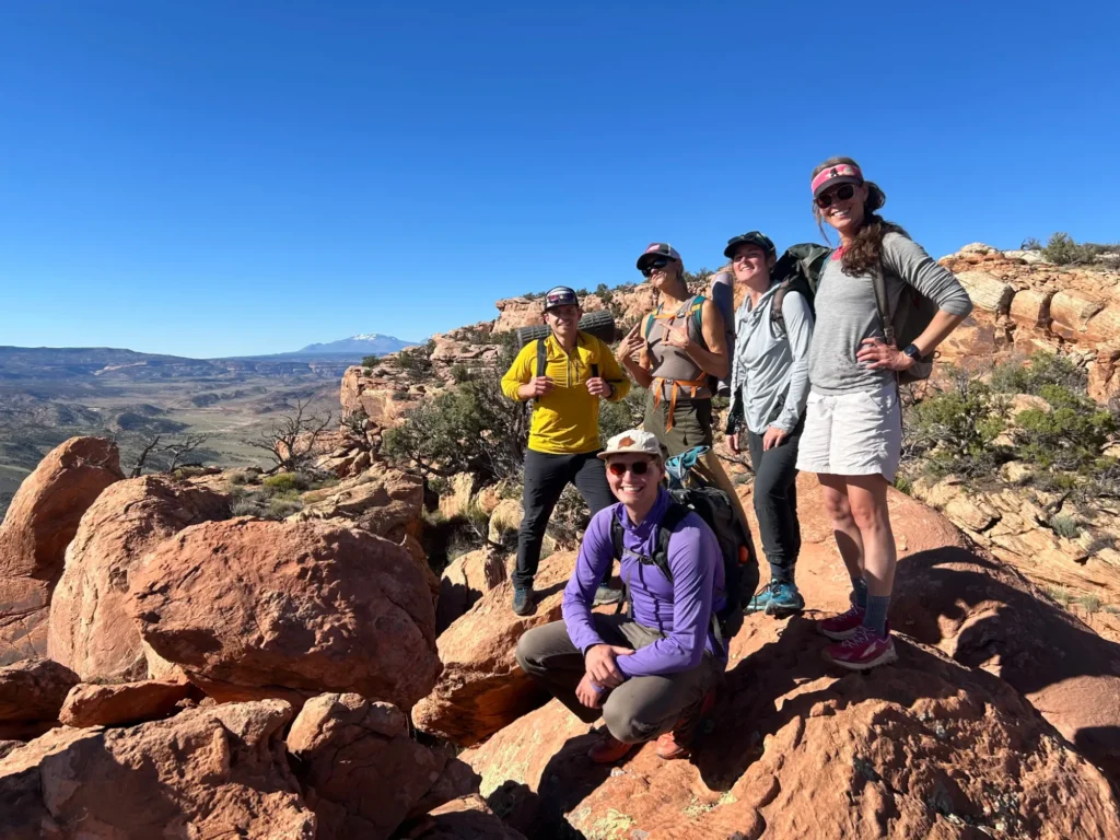 A LifeWays group smiling on red sandstone boulders above a wide desert valley